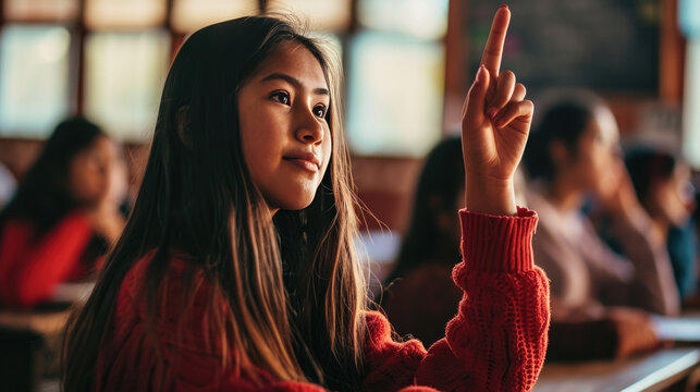Young female student is raising her hand to answer a question in a classroom setting