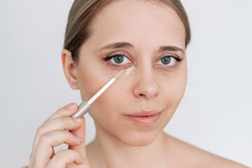 Close-up of a young caucasian attractive blonde woman applying the concealer for dark eyes. Bruises under the eyes. Foundation cream hiding spot imperfections on female face