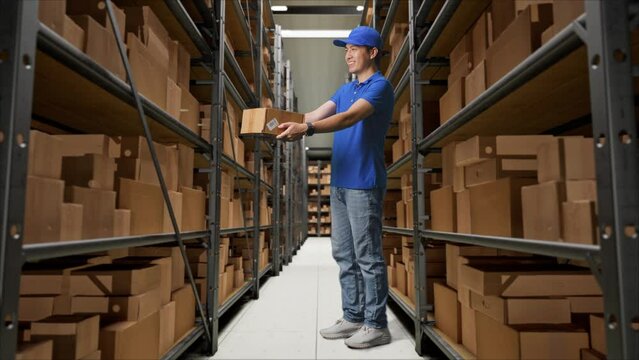 Full Body Of male Giving A Carton To Someone And Smiling While Delivering It In Warehouse
