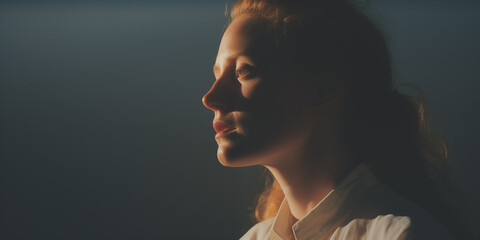Intense profile of a woman with her face half-illuminated by golden light - obrazy, fototapety, plakaty