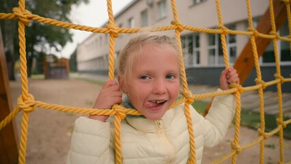 Little cute European girl playing on playground show tongue smiling joy fun schoolgirl child city outside street childhood amusement sporty happy leisure enjoyment activity kid learner pupil adventure