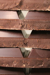 A stack of extra dark bitter chocolate bar pieces stacked in horizontal rows close up. Vertical...
