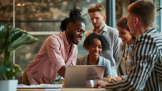 Diverse Group Of Four Young Professionals Or Friends, Gathered Around A Laptop At A Modern Workspace, Collaborating Or Discussing