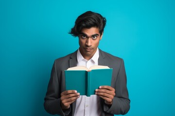 young indian student with books holds on a blue studio background. education.