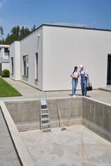 Woman and repairman talking and watching empty swimming pool before repair