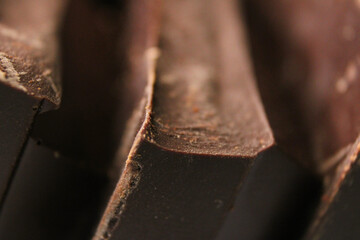 Pieces of extra dark bitter chocolate bar stacked in vertical slanted rows close up.