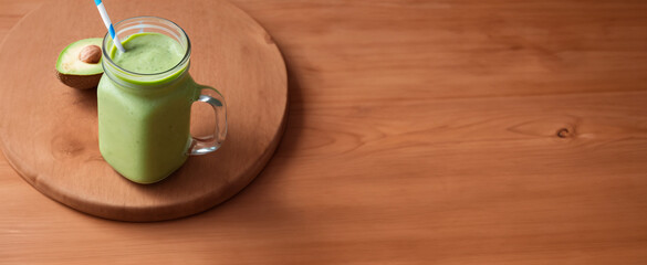 Vitamina de Abacate com leite no copo de vidro com uma banda de abacate ao lado, servido sobre uma mesa de madeira. - obrazy, fototapety, plakaty