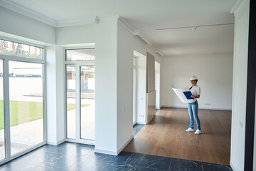 Fototapeta premium Smiling female designer watching blueprint and looking at new modern townhouse