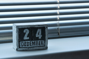 Morning December 24 on wooden calendar standing on window with blinds.