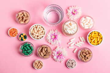 Many vitamins, dietary supplements, pills, meds, capsules and tablets in small jars, pink flowers...