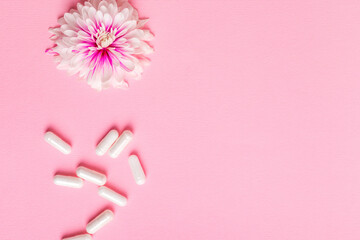 Horizontal photo of vitamin capsules and pink flower from above on a pink background. Healthy...