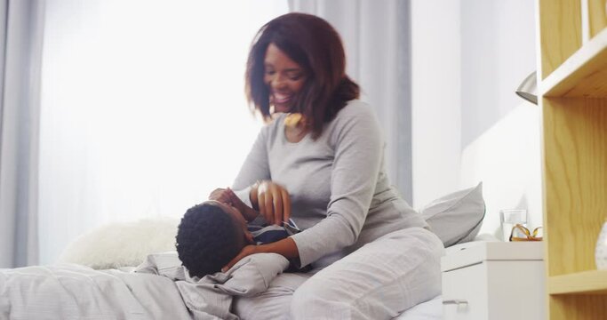 Hug, tickle and mother with boy child on a bed happy, playful and having fun in their home together. Black family, love and mom with kid in bedroom embrace, smile and bonding on vacation in a house