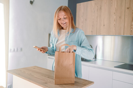 Online home food delivery. Woman checking her online order list on her phone. Young woman unpacking boxes of food at home. Start of a healthy life. High quality photo