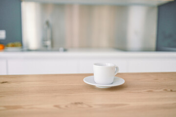 Cup of tea or coffee on wooden table in contemporary kitchen interior. Kitchen appliances and decor on background.