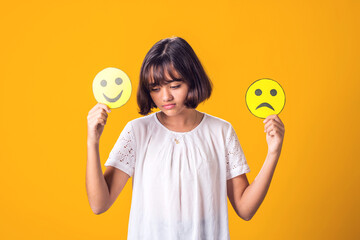 Upset girl holds emoticons with happy and sad emotions.