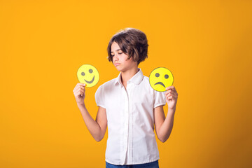 Upset girl holds emoticons with happy and sad emotions.