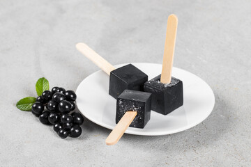 Black Matcha Ice Cream in the shape of a mini cube on a wooden stick. On a plate. Close-up	