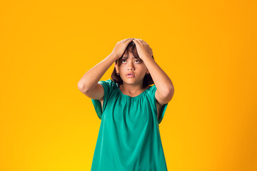 Sad kid girl holding her head over yellow background. Frustration concept