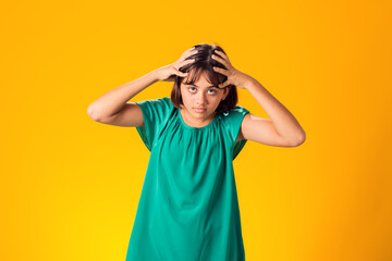 Sad kid girl holding her head over yellow background. Frustration concept