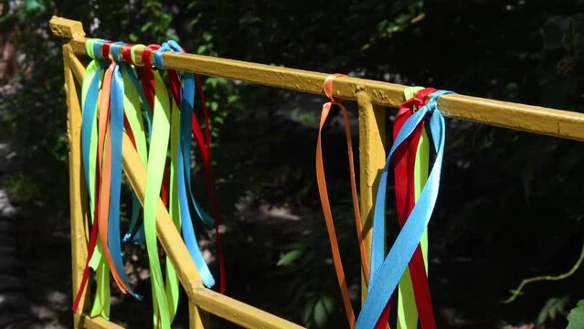 Various color satin ribbons tied at yellow fence shake in wind. Summer fun background of ribbon garlands outdoor