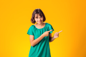 Smiling child pointing hand at space over yellow background - obrazy, fototapety, plakaty