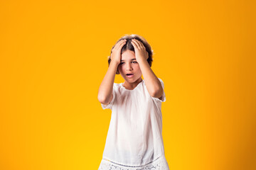 Sad kid girl holding her head over yellow background. Frustration concept