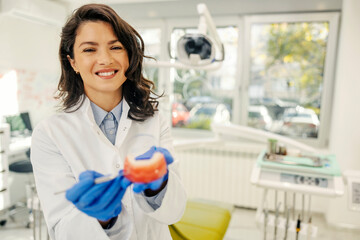 Portrait of a happy dentist holding a jaw model and explaining oral health.