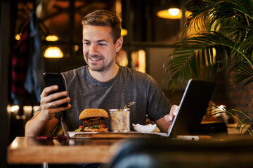 A busy casual man is sitting in restaurant on a lunch break and using technologies for business.