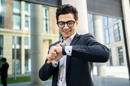 Smiling businessman checking time on smartwatch in urban setting, showcasing technology and punctuality.