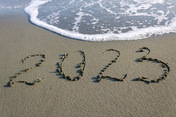Foamy sea wave erasing number 2023 written on beach sand 