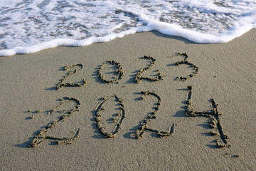 Numbers 2023 and 2024 written on beach sand 