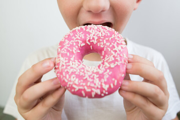 close-up of a boy eating a delicious donut with pink icing.