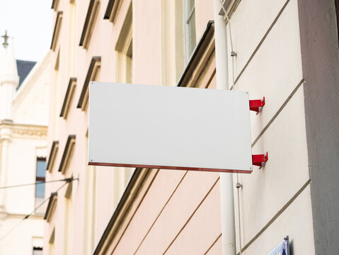 Small store sign template on a house. A white space for a logo or icon. The name of the business or opening hours could be displayed. Signage mock up of a retailer in a town.