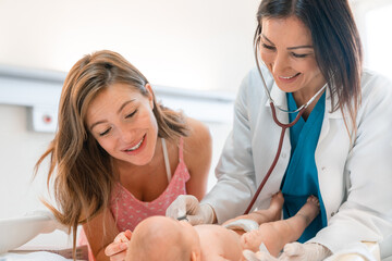 Smiling female pediatrician examining newborn baby with stethoscope while the mother is standing...