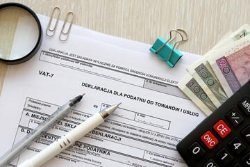 Declaration for tax on goods and services VAT-7 form on accountant table with pen and polish zloty money bills close up