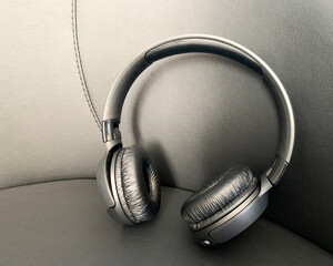 Modern wireless black ambi earphones on a black leather sofa.