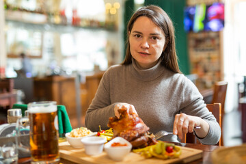 Female traveler tasting fried pork ham knuckle traditionally served with stewed cabbage, pickled...