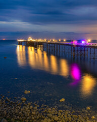 Long historic pleasure pier at dusk with lights reflecting in the water. Llandudno seaside resort, North Wales