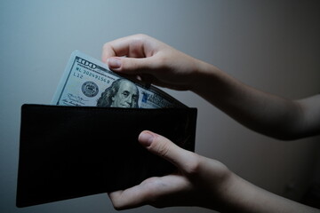 Woman puts 100 dollar banknote inside a wallet 