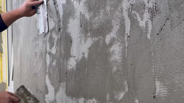Close-up of a worker's hand with a trowel. Applying mortar to reinforcing mesh and rigid polyurethane foam for home insulation. Exterior construction works.