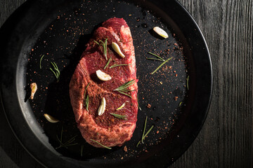 Raw Ribeye steak with spices on a black plate on a wooden table.