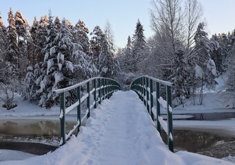 Snow-covered bridge over an icy river in a winter park