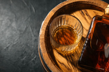 Wooden barrel with glass and bottle of tasty whiskey on dark background