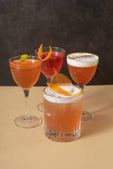 Four bright alcoholic cocktails in glasses on dark beige background.
