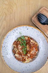 Bolognese in a bowl decorated dry tomato and microgreen on a wooden table top view, flat lay