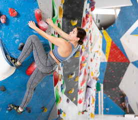 Focused sporty young girl climbing on bouldering wall demonstrating physical strength, technical...