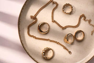 Plate with golden rings and necklace on white background