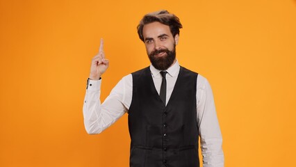 In formal restaurant clothes, employee indicating upward and signals at something over his head. Skilled young butler gives direction recommendation in studio, feeling confident.