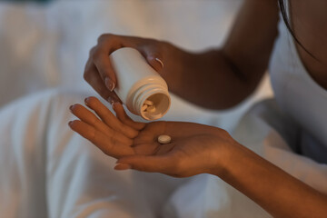 Young woman taking pill in bedroom at night, closeup