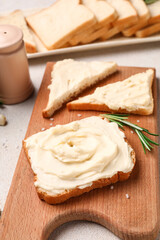 Wooden board of tasty toasts with cream cheese on light background